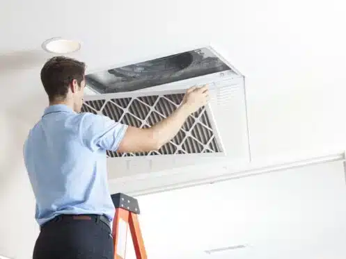 Man cleaning duct in living room while standing on ladder