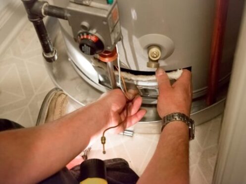 A man uses a flashlight to help him see the hot water heater in a dark closet