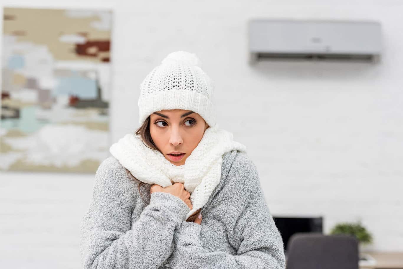 woman wearing jacket, scarf and hat inside because heater is broken and needs repair