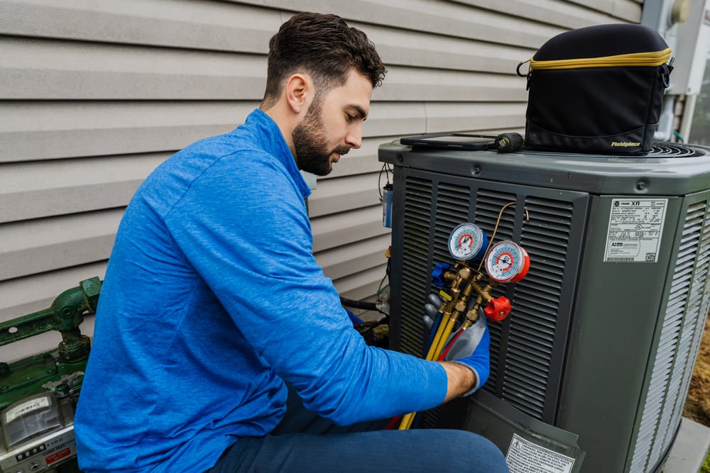 HVAC technician conducting air conditioning services on an outdoor unit.