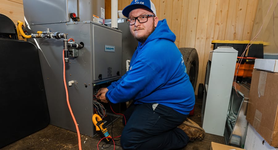 Technician kneeling in front of furnace perfuming maintenance.
